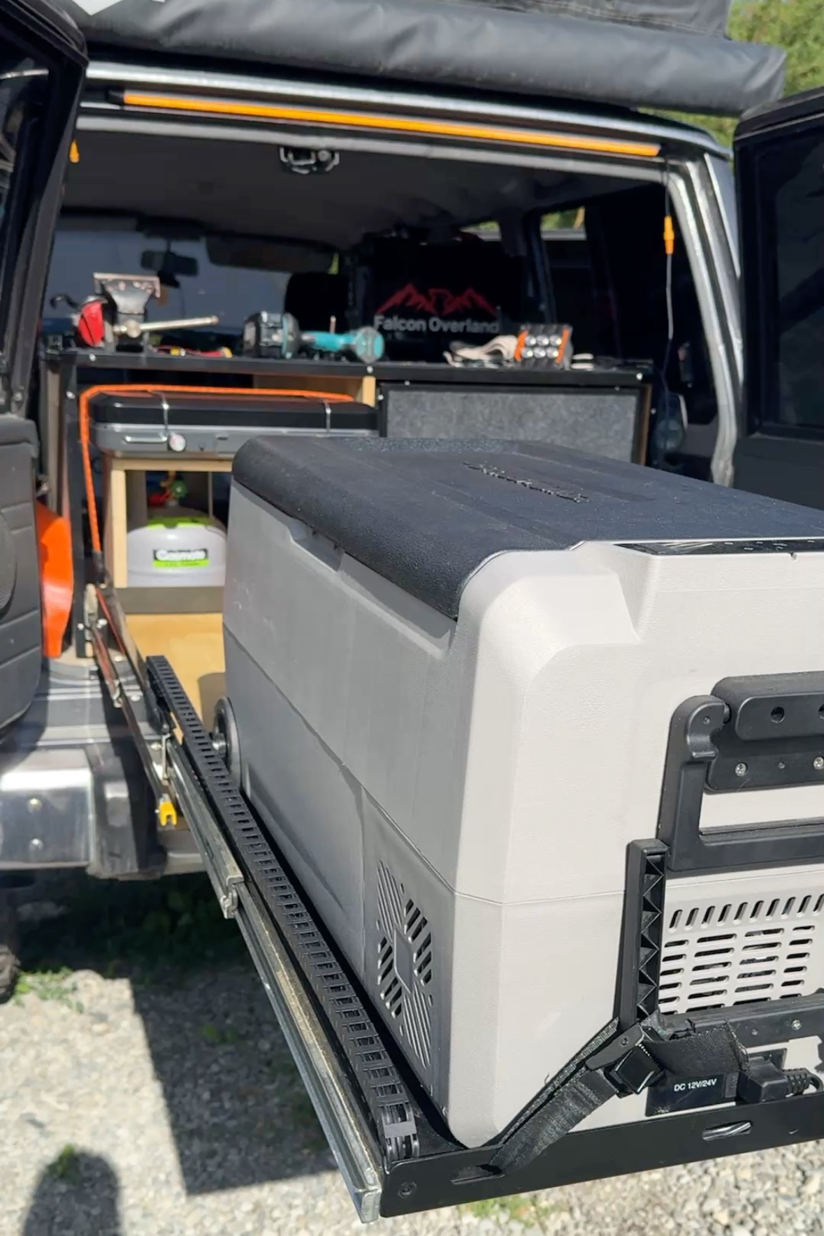 Portable fridge extended from the rear of a vehicle with a cable chain along the slide