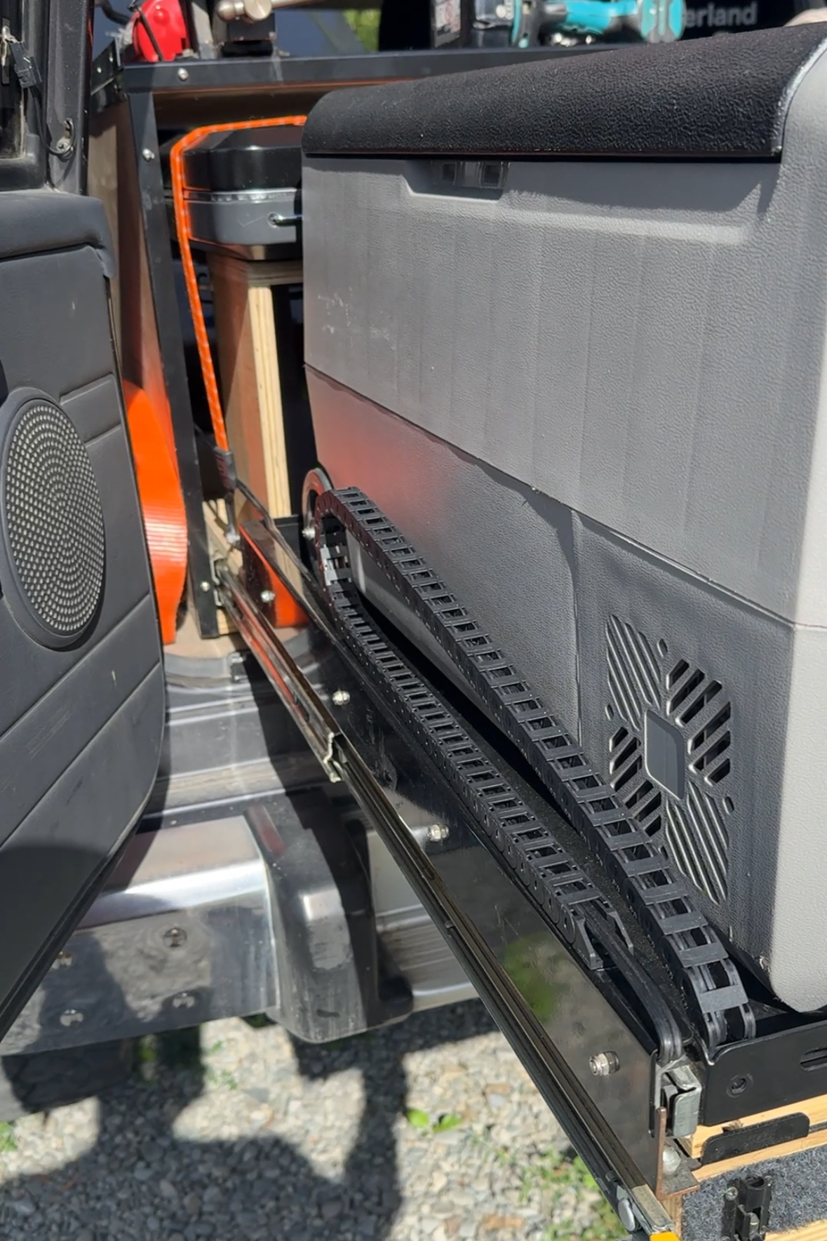 Side view of a cable chain fitted beside a portable fridge on an extended vehicle slide