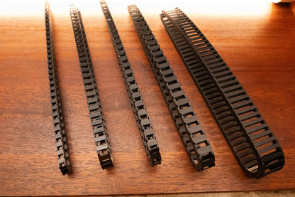 Black fridge slide cable chains in several widths arranged on a wooden surface